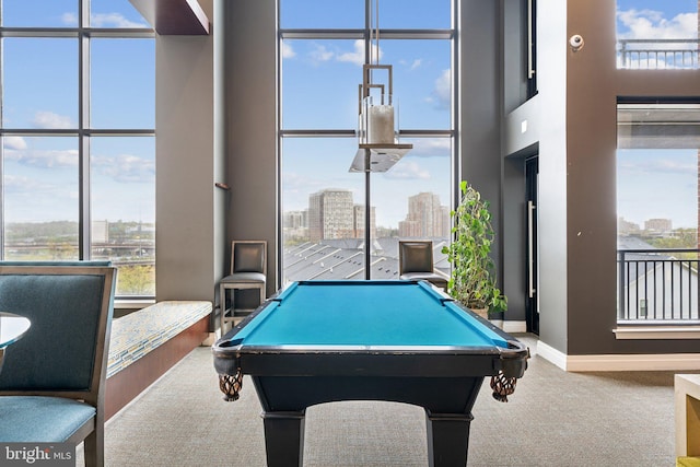 recreation room featuring a healthy amount of sunlight, a city view, baseboards, and carpet floors