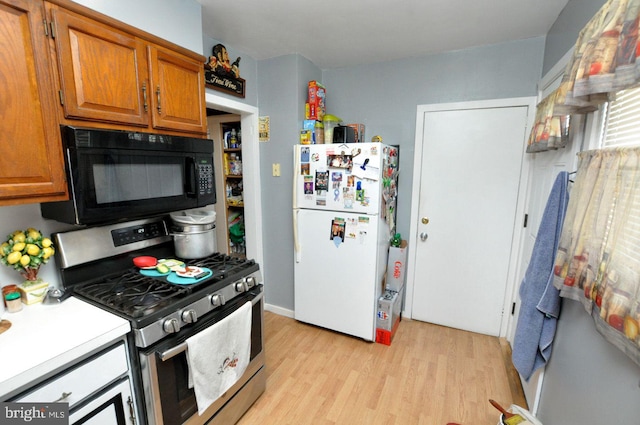 kitchen with light wood-type flooring, freestanding refrigerator, black microwave, brown cabinetry, and gas stove