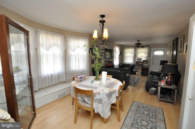 dining space featuring light wood-style floors and ceiling fan with notable chandelier