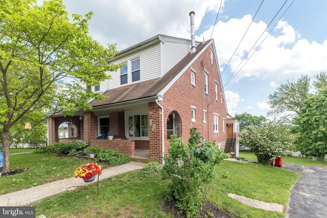 view of front of house with brick siding, a front yard, a porch, and roof with shingles
