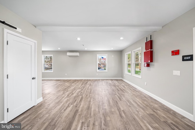 empty room with a wall mounted AC, a barn door, light wood-style flooring, and baseboards
