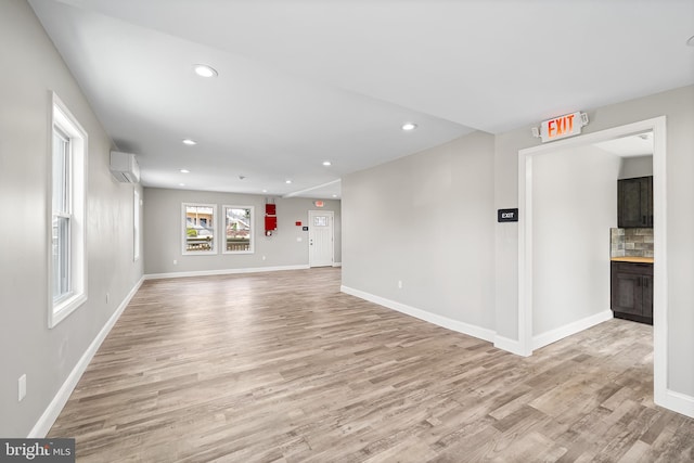 unfurnished living room featuring light wood-type flooring, a wall unit AC, baseboards, and recessed lighting