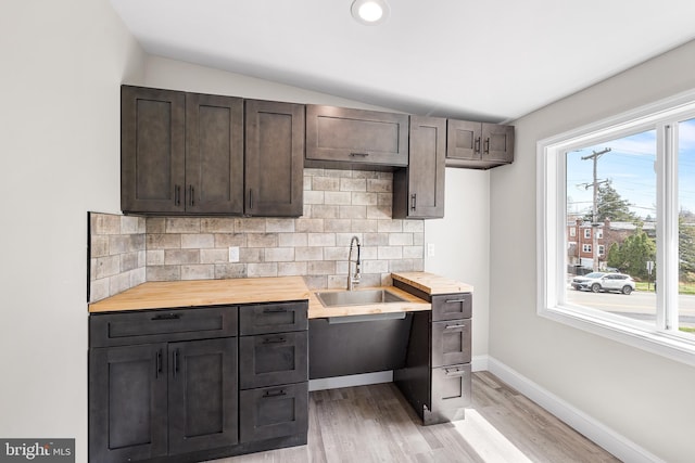 kitchen with light wood-style flooring, baseboards, a sink, dark brown cabinetry, and decorative backsplash