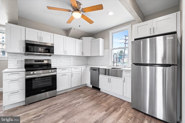 kitchen with light wood-style flooring, a sink, light countertops, stainless steel appliances, and backsplash
