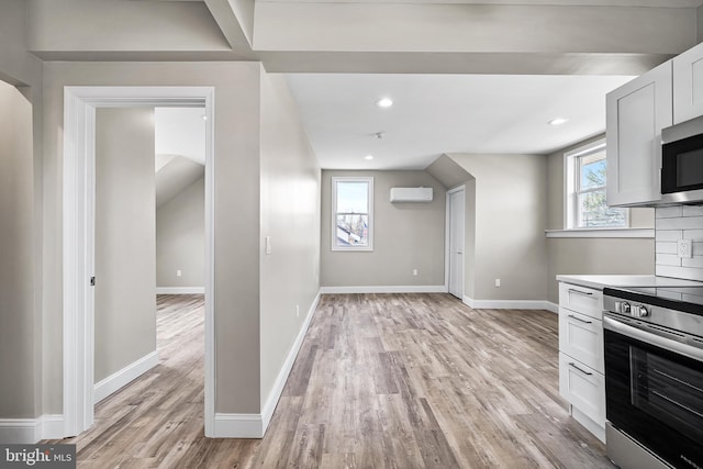 kitchen with baseboards, a wall mounted air conditioner, light countertops, light wood-style floors, and stainless steel appliances