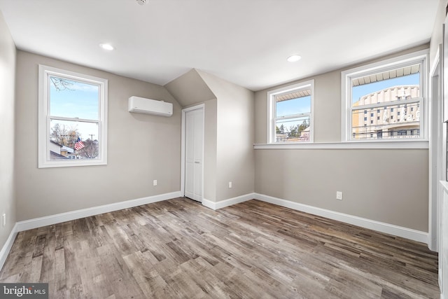 unfurnished bedroom with baseboards, multiple windows, wood finished floors, and a wall unit AC