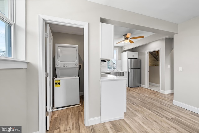 laundry area with baseboards, stacked washer and dryer, light wood-style floors, laundry area, and ceiling fan