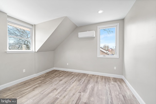 additional living space with baseboards, vaulted ceiling, wood finished floors, and a wall mounted air conditioner