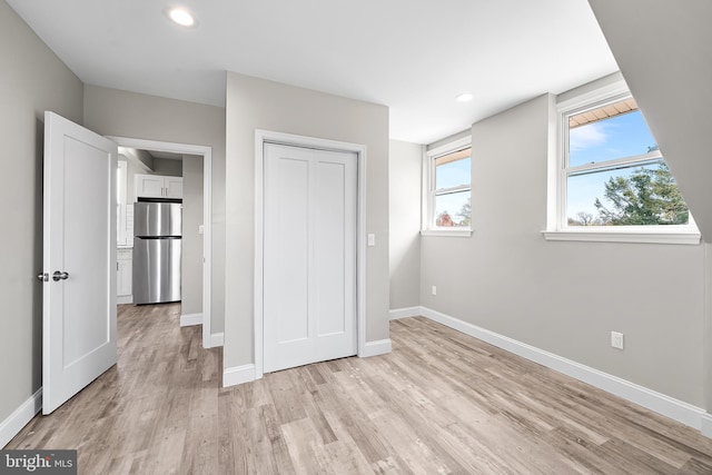unfurnished bedroom with freestanding refrigerator, light wood-type flooring, a closet, recessed lighting, and baseboards