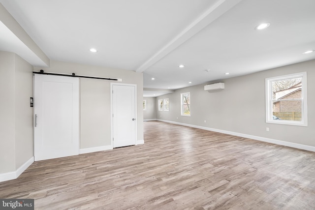 below grade area featuring a wall mounted AC, baseboards, recessed lighting, a barn door, and light wood finished floors