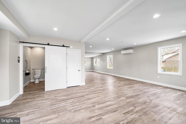 basement featuring a wall mounted AC, baseboards, recessed lighting, a barn door, and light wood finished floors