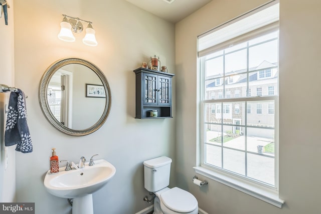 half bath with a sink, toilet, a chandelier, and baseboards