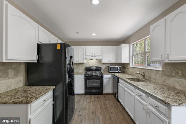 kitchen with a sink, under cabinet range hood, decorative backsplash, black appliances, and white cabinets