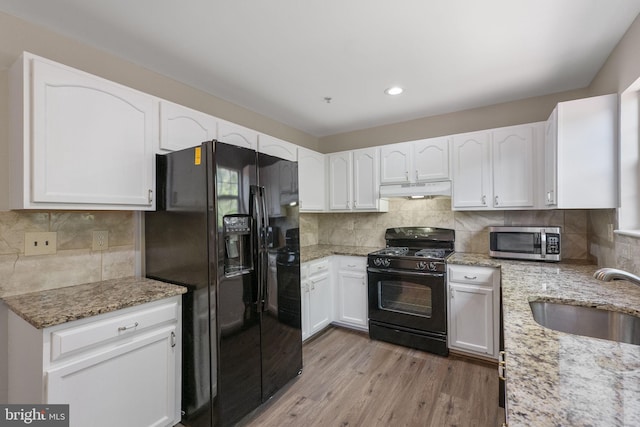 kitchen featuring light stone countertops, black appliances, under cabinet range hood, and a sink