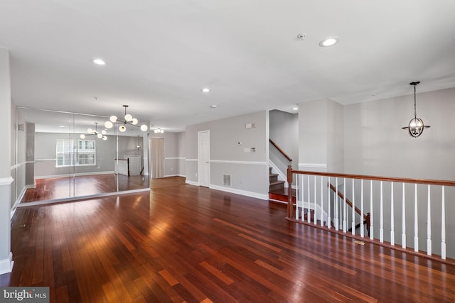 unfurnished living room with a chandelier, baseboards, hardwood / wood-style floors, and stairway