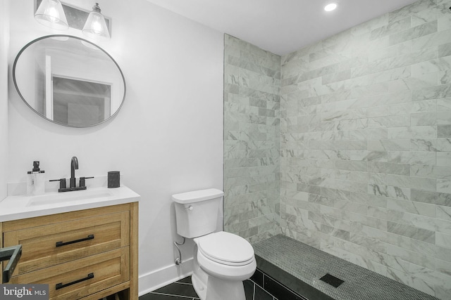 bathroom with baseboards, toilet, vanity, tiled shower, and tile patterned flooring
