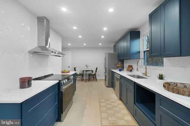 kitchen featuring a sink, wall chimney range hood, light wood finished floors, stainless steel appliances, and backsplash