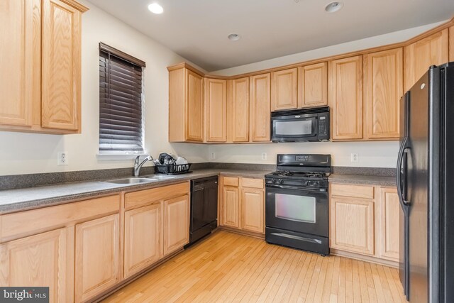 kitchen with a sink, light brown cabinets, black appliances, and dark countertops