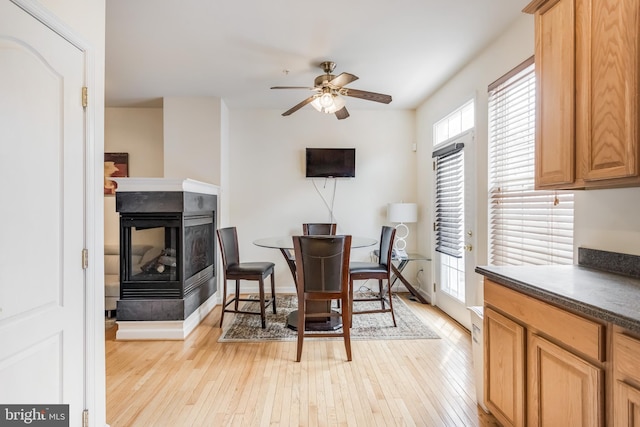 dining space with a multi sided fireplace, light wood-style floors, and a ceiling fan