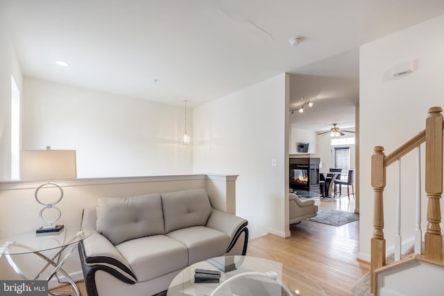 living room with light wood-style floors, ceiling fan, a multi sided fireplace, stairs, and baseboards