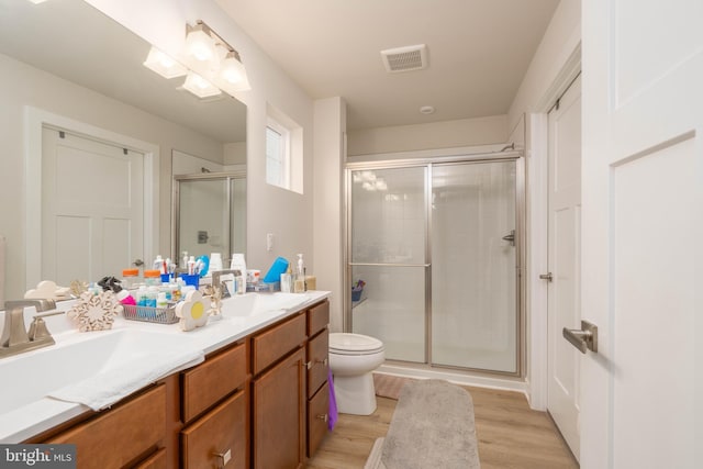 bathroom with double vanity, a stall shower, toilet, visible vents, and wood finished floors