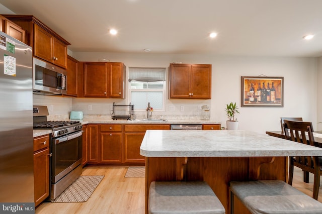 kitchen featuring a sink, light countertops, light wood-type flooring, stainless steel appliances, and a breakfast bar area