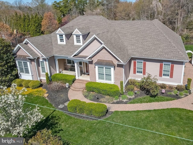 view of front of home featuring brick siding, roof with shingles, and a front yard