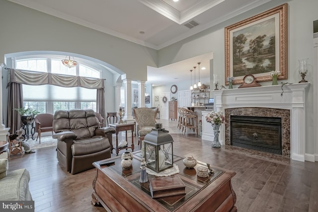 living area featuring a towering ceiling, visible vents, ornate columns, wood finished floors, and ornamental molding