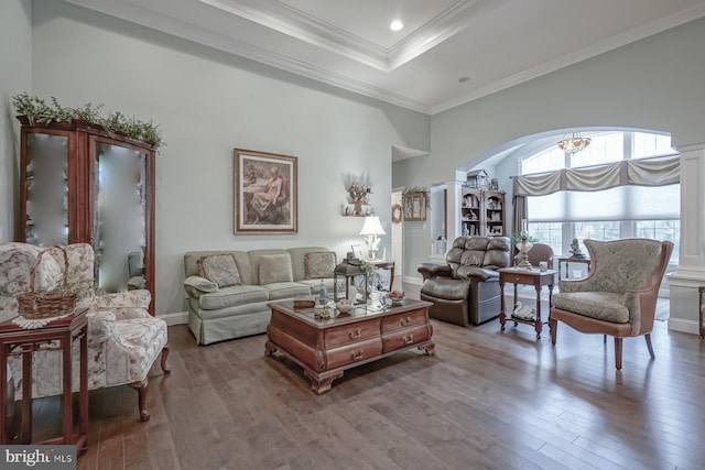 living area featuring a high ceiling, a tray ceiling, wood-type flooring, arched walkways, and a notable chandelier