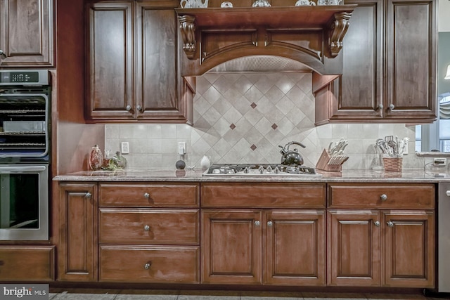 kitchen with light stone counters, tasteful backsplash, stainless steel appliances, and custom range hood