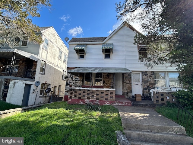 view of front of home with a front lawn, stone siding, and covered porch