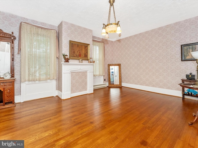 36 Fulton Ave, Walkersville, MD 21793 - unfurnished living room with a notable chandelier, baseboard heating, wallpapered walls, baseboards, and wood finished floors