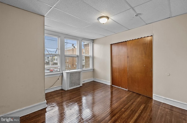 unfurnished bedroom with a closet, hardwood / wood-style flooring, baseboards, and a drop ceiling