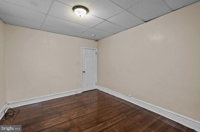 unfurnished room featuring dark wood-type flooring, a paneled ceiling, and baseboards