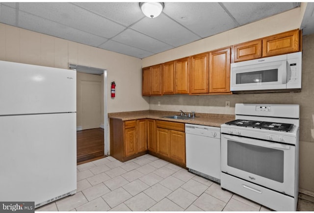 kitchen with white appliances, light tile patterned flooring, brown cabinets, a drop ceiling, and a sink