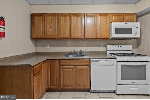 kitchen featuring brown cabinetry, white appliances, a paneled ceiling, and a sink