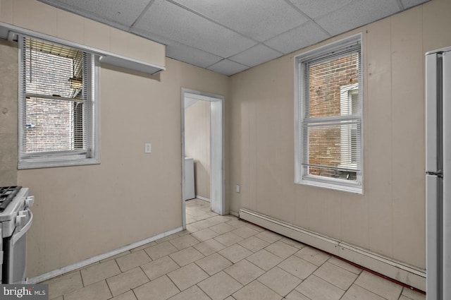unfurnished room featuring light tile patterned flooring, a baseboard heating unit, and a drop ceiling
