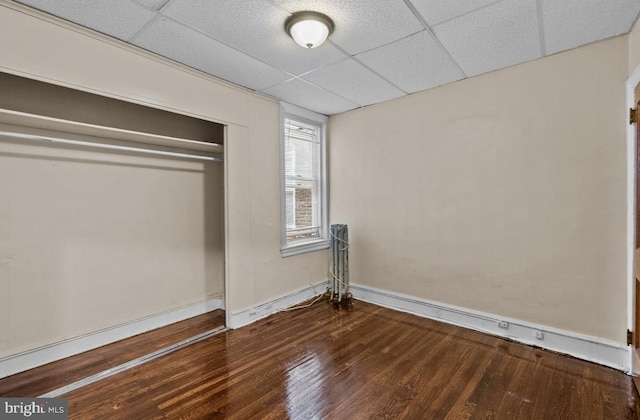 unfurnished bedroom featuring wood finished floors, a closet, a drop ceiling, and baseboards