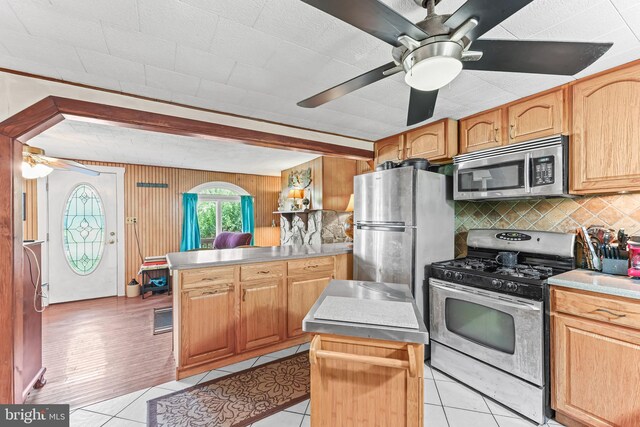kitchen featuring decorative backsplash, appliances with stainless steel finishes, a ceiling fan, a peninsula, and light tile patterned flooring