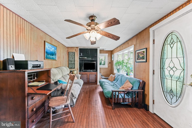 living room featuring wood walls, ceiling fan, and wood-type flooring