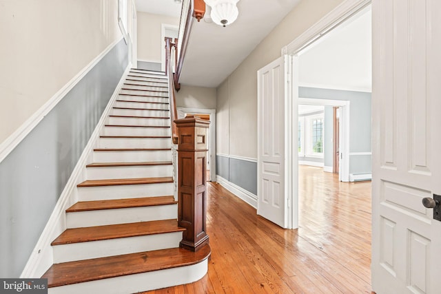 stairway featuring a baseboard heating unit, baseboards, and hardwood / wood-style flooring