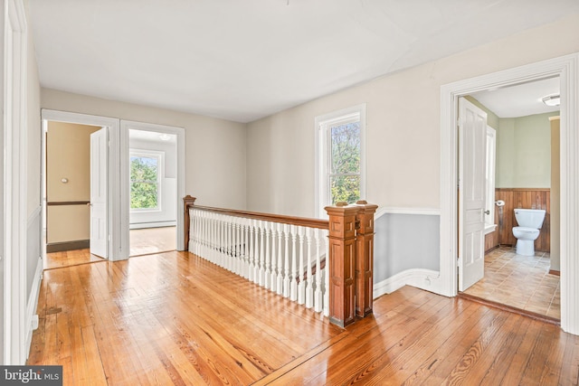 interior space with baseboards, a baseboard heating unit, light wood finished floors, wainscoting, and an upstairs landing
