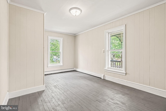unfurnished room featuring hardwood / wood-style floors, a baseboard heating unit, ornamental molding, wooden walls, and baseboards