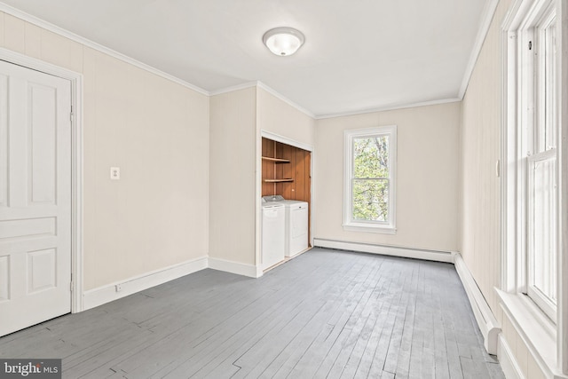 unfurnished living room with wood finished floors, a baseboard heating unit, crown molding, washing machine and dryer, and baseboards