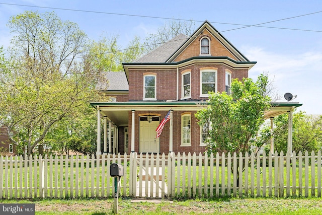 view of front facade with covered porch, roof with shingles, brick siding, a front yard, and a fenced front yard
