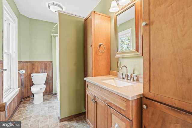 full bathroom featuring toilet, a shower, vanity, wooden walls, and wainscoting