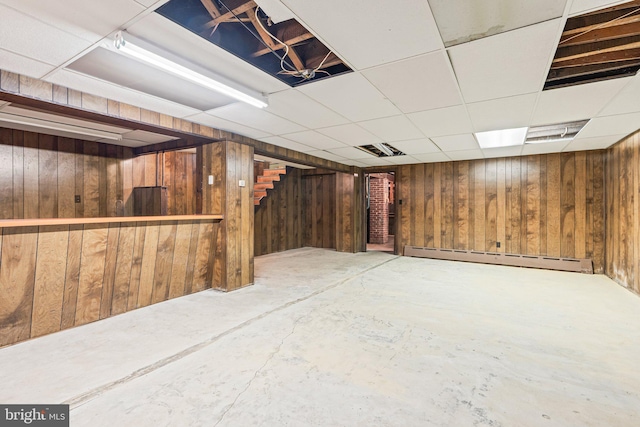 finished below grade area with wood walls, a baseboard radiator, stairway, and a paneled ceiling