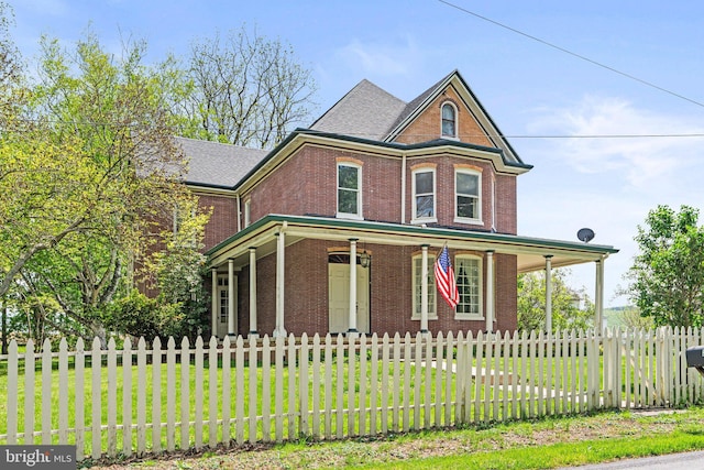 victorian-style house with covered porch, a fenced front yard, brick siding, and a front yard