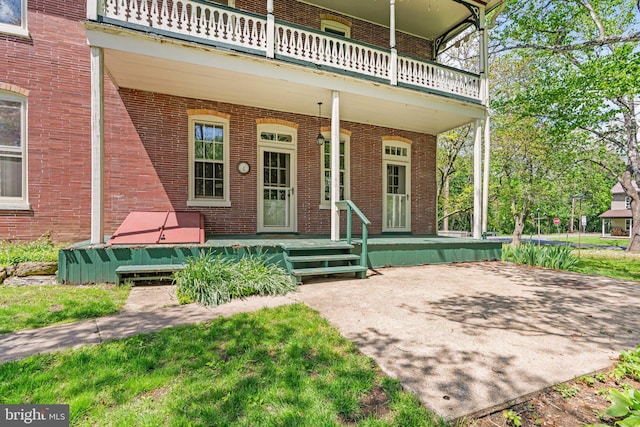 view of exterior entry featuring a balcony, brick siding, and covered porch