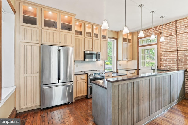 kitchen with dark wood finished floors, high quality appliances, cream cabinetry, and tasteful backsplash